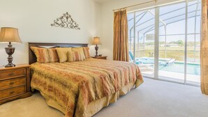 A bedroom with a large bed, two bedside tables with lamps, a decorative wall piece, and a large window with a view of a swimming pool. - Marbella 1020 (Davenport)