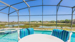 A pool area with two chairs and a table, surrounded by a metal fence, overlooking a water body and distant buildings. - Marbella 1020 (Davenport)