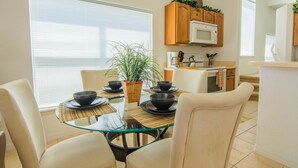 Una cocina moderna con armarios de madera, un microondas y un comedor con mesa y sillas de vidrio.