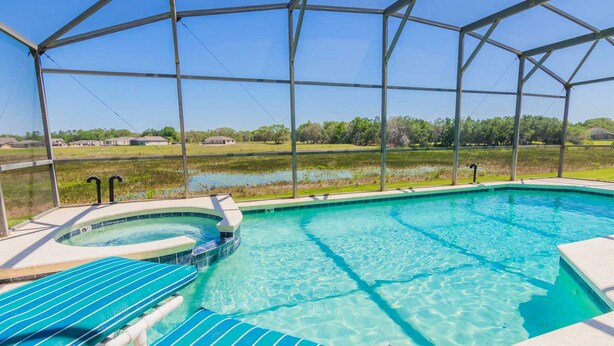 Una piscina cristalina con jacuzzi, rodeada por una zona techada con sillones de descanso.