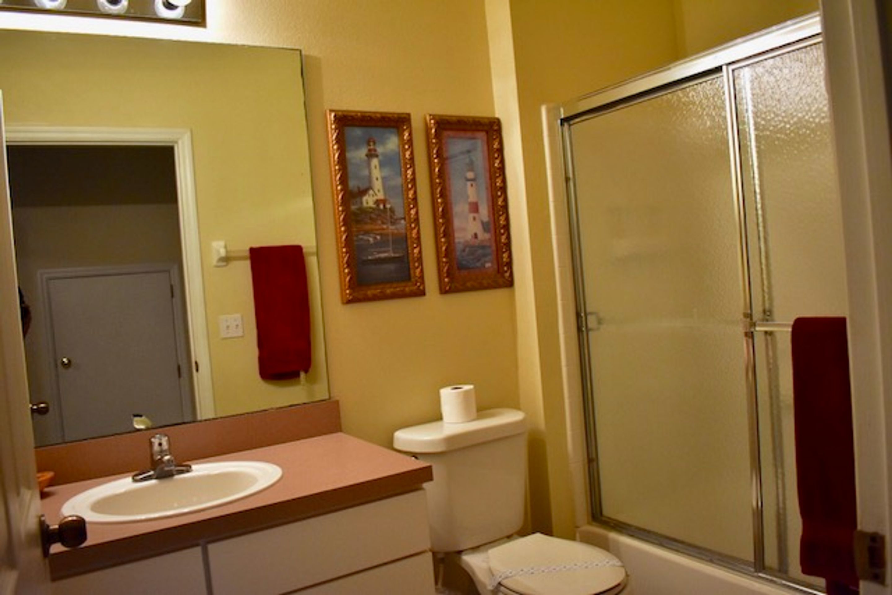 A bathroom with a sink, toilet, and glass shower enclosure. There are two framed pictures on the wall.