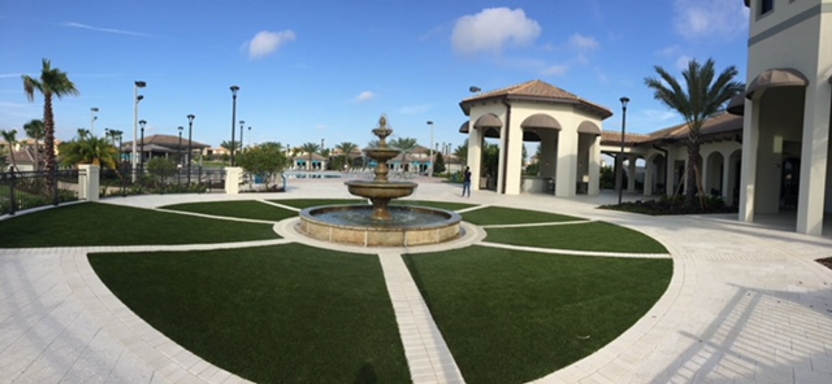 A courtyard with a central fountain, surrounded by a well-maintained lawn and a building with a tiled roof.