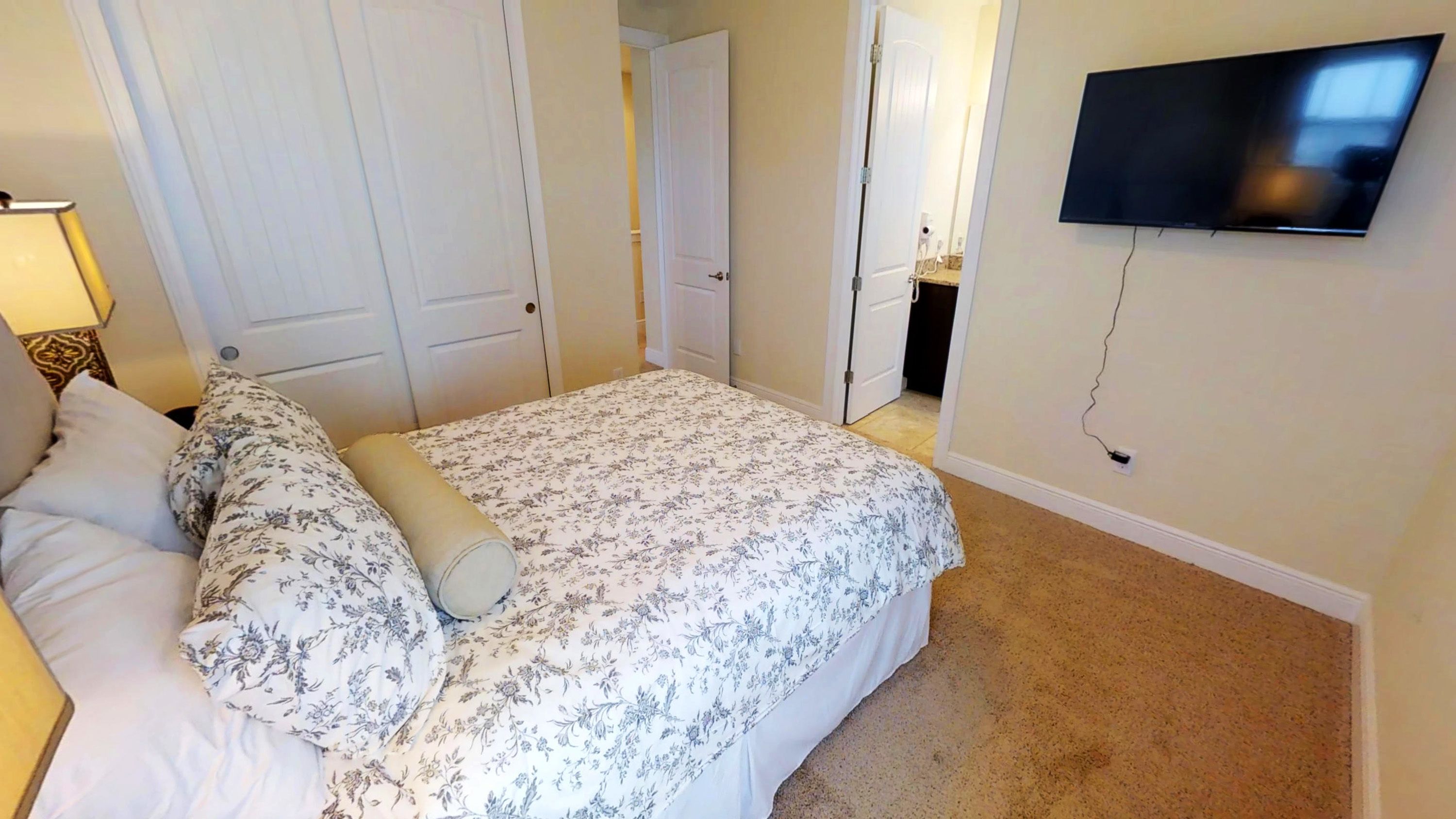 A bedroom with a bed, a TV mounted on the wall, and a door leading to another room.