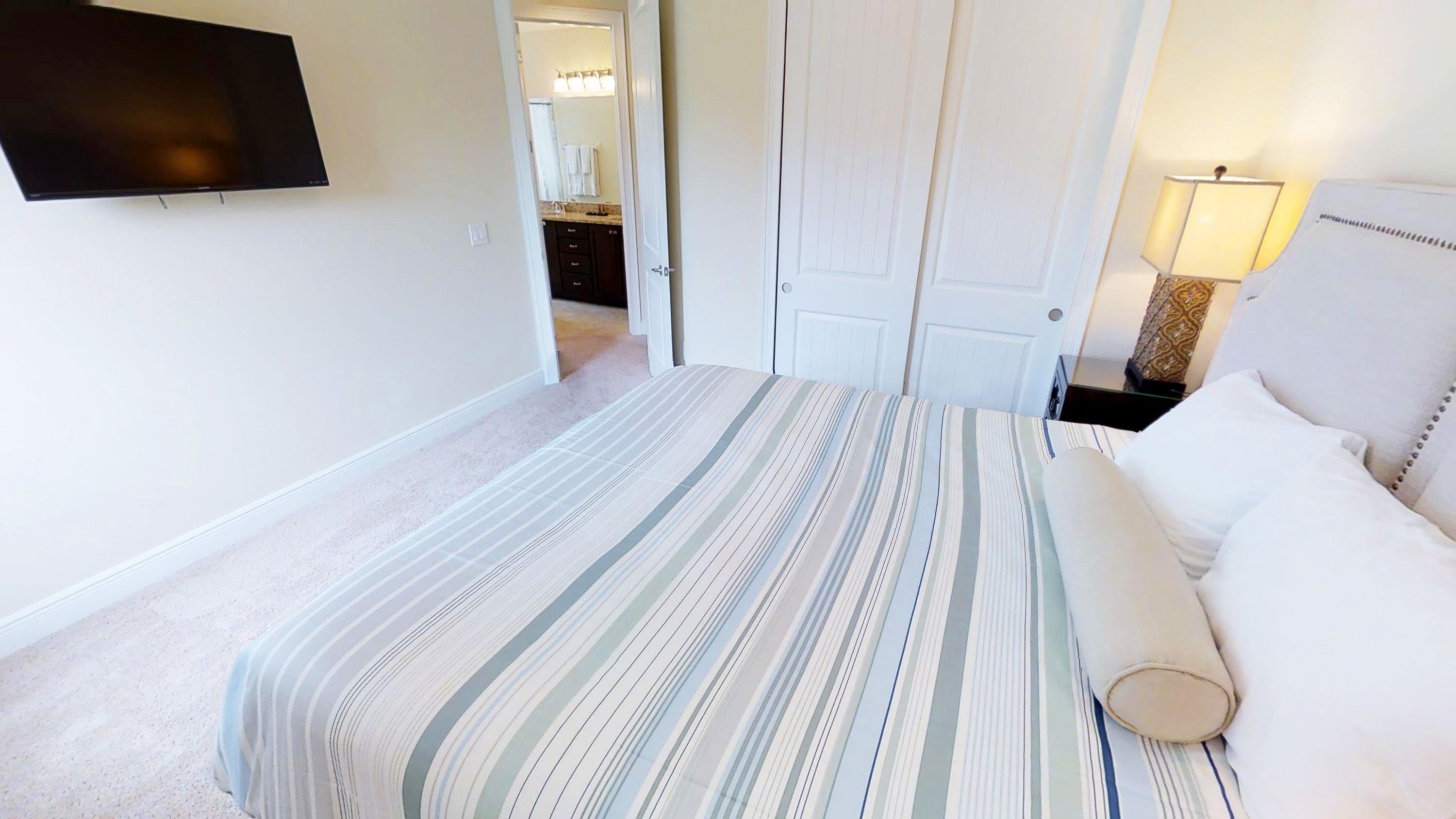 A bedroom with a bed, a TV mounted on the wall, a door, and a lamp.