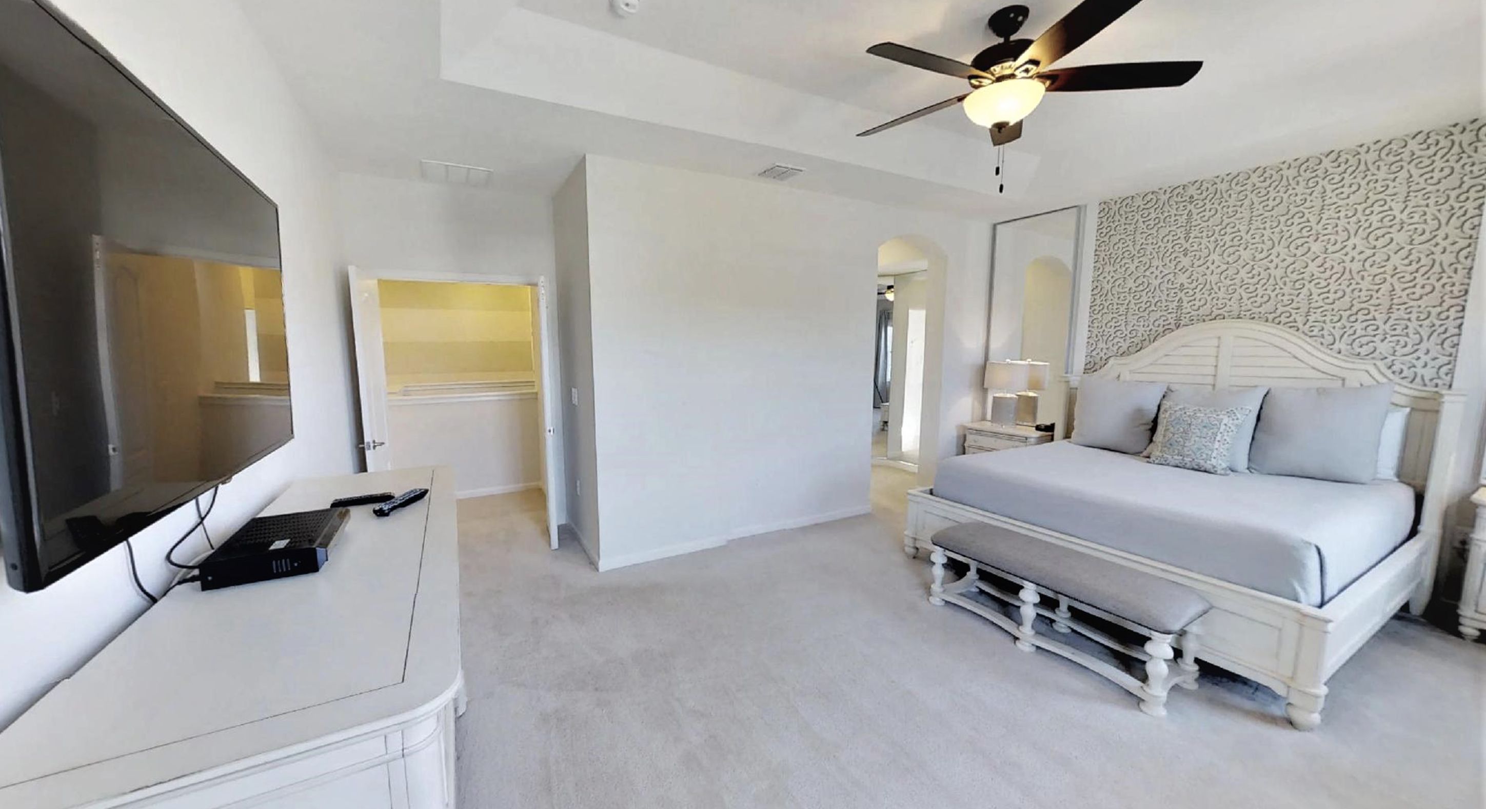 A bedroom with a bed, a desk, a TV, and a ceiling fan.