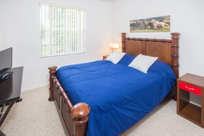 Quarto com cama de madeira, escrivaninha, luminária e janela com persianas.