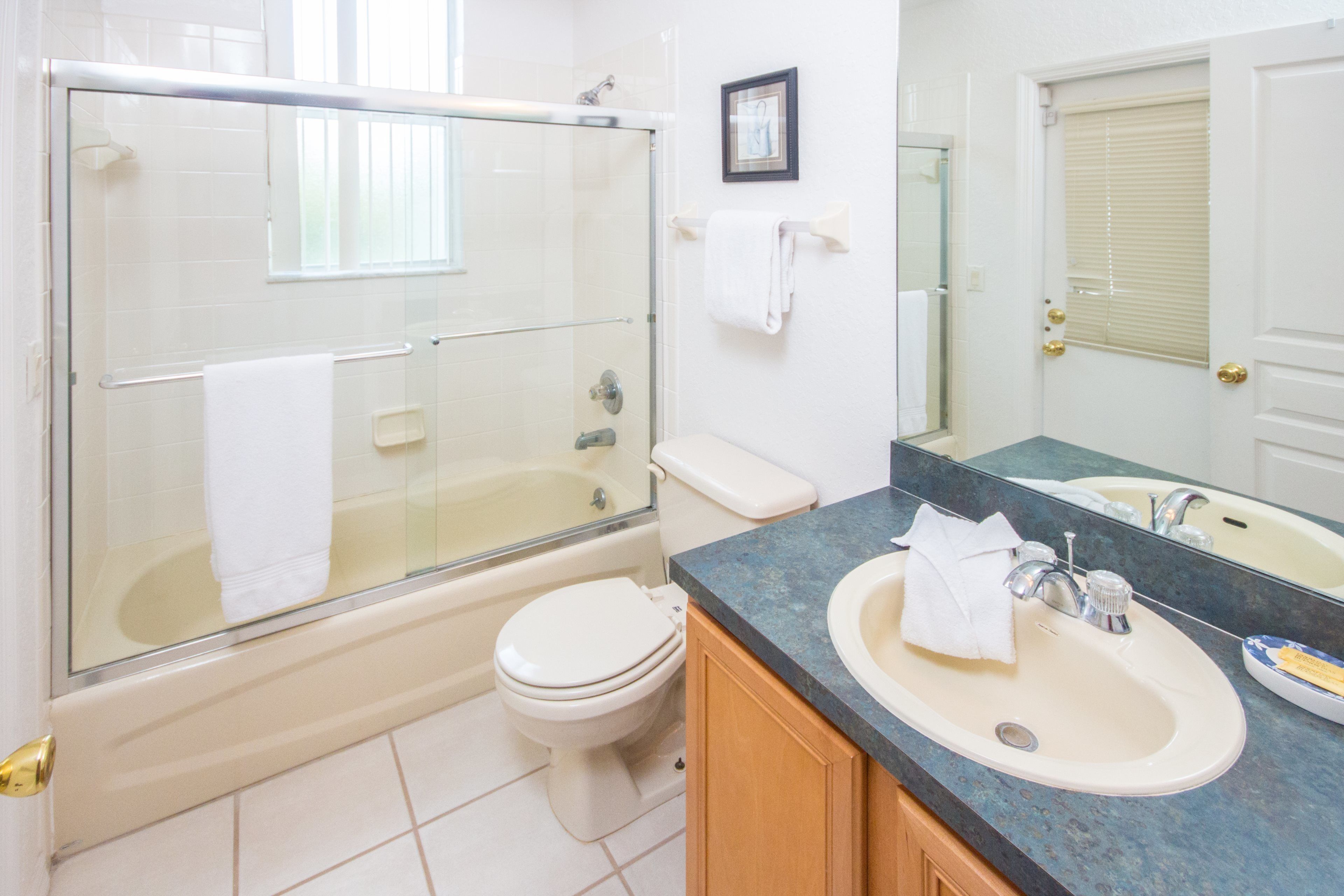 A bathroom with a glass-enclosed shower, a white toilet, a sink with a mirror, and a towel hanging on the wall.
