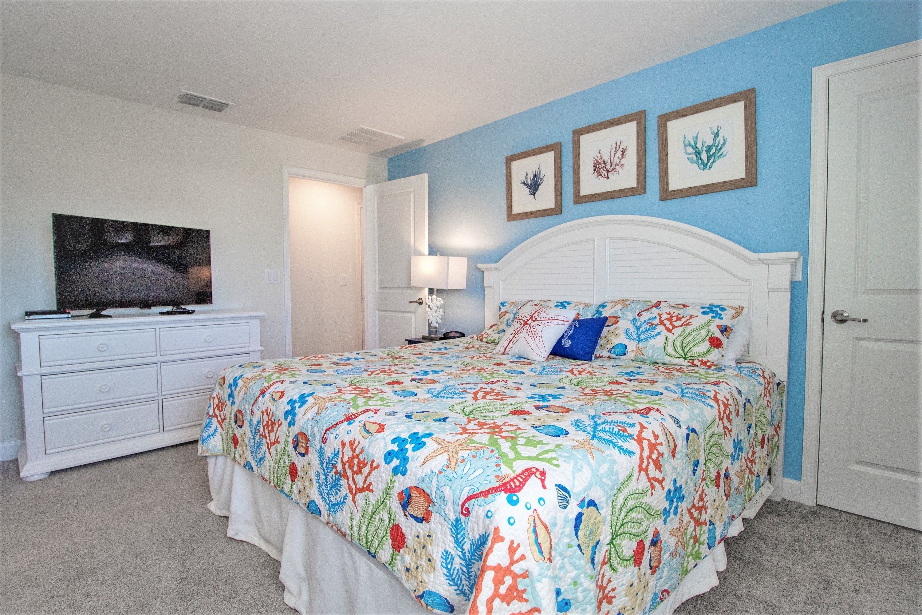 Un dormitorio con cama, cómoda, televisor y cuadros en la pared.