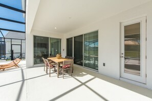 A modern outdoor patio with a dining table and chairs, large sliding glass doors, and a view of the surrounding area. - Sonoma Resort 2682 (Kissimmee)