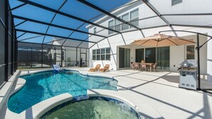 Ein Schwimmbecken mit Whirlpool, Liegestühlen und einer überdachten Terrasse mit Tisch und Stühlen.