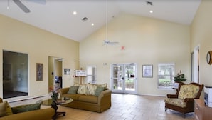 A spacious living room with a high ceiling, a ceiling fan, and a large sliding glass door leading to a patio. - Club Cortile 2730a (Kissimmee)