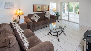 A living room with a brown sofa set, a glass coffee table, and a ceiling fan. - Club Cortile 2730a (Kissimmee)