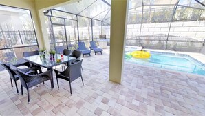 A covered outdoor area with a pool, lounge chairs, and a table with chairs. - Encore Resort at Reunion 7407 (Kissimmee)
