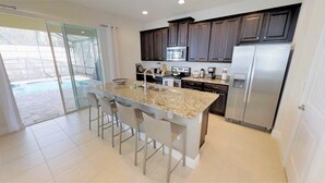 A modern kitchen with dark cabinets, stainless steel appliances, and a large island with bar stools. - Encore Resort at Reunion 7407 (Kissimmee)