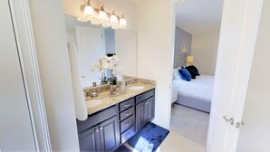A bathroom with a granite countertop, a sink, and a mirror. There is a door leading to a bedroom with a bed and a nightstand. - Encore Resort at Reunion 7407 (Kissimmee)