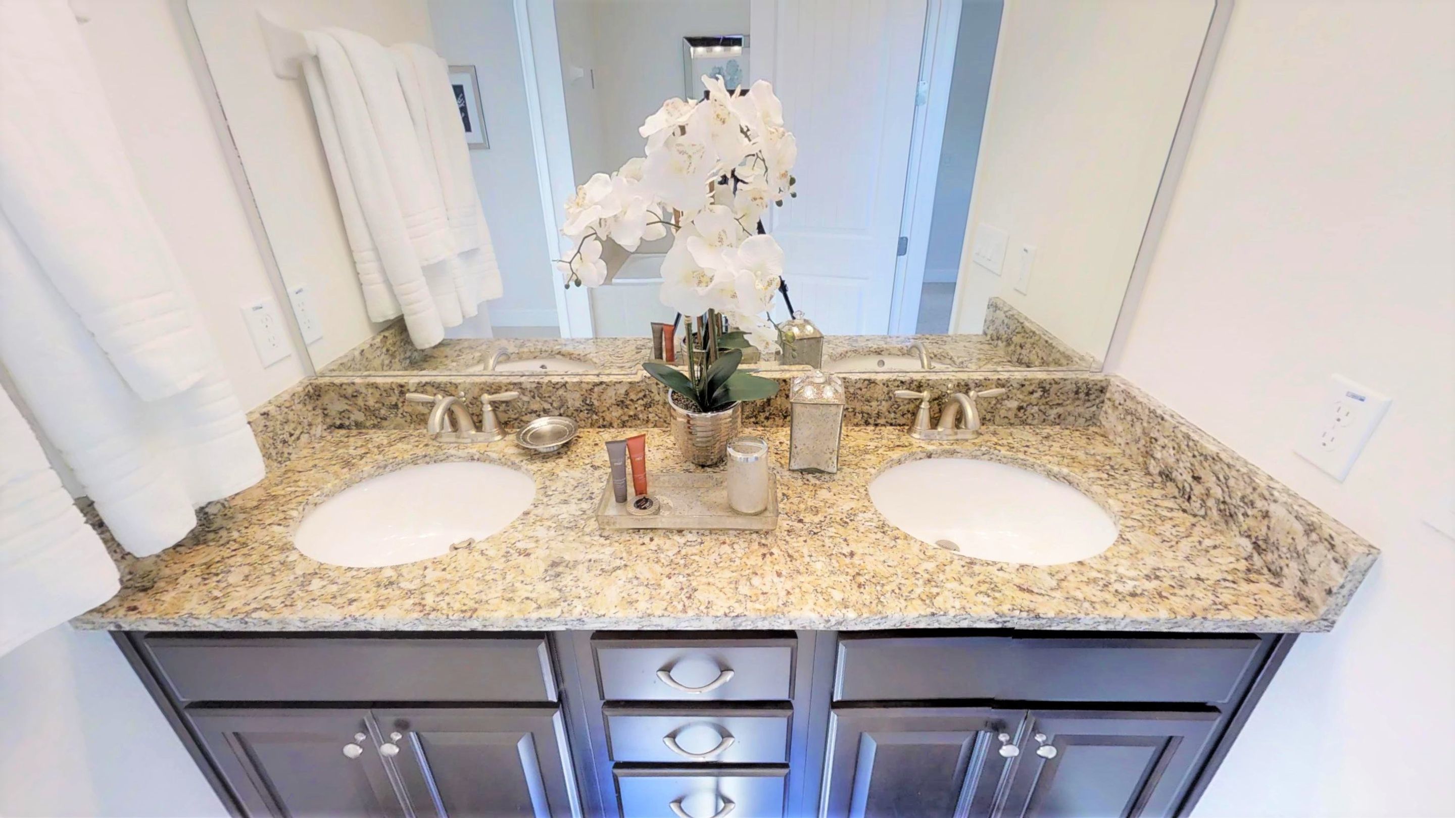 A bathroom with two sinks, granite countertops, and dark cabinetry.