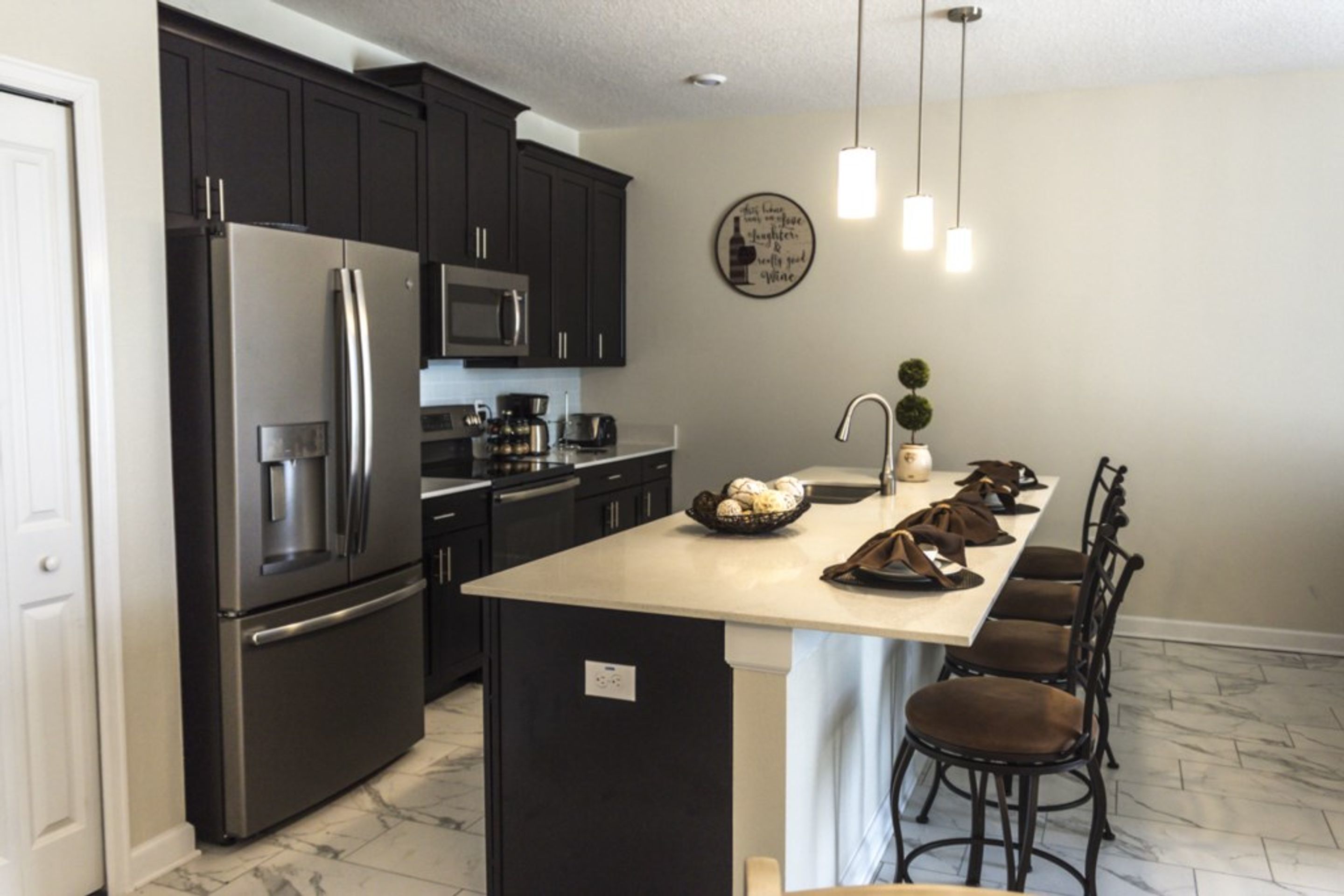 A modern kitchen with dark cabinets, stainless steel appliances, a large island with seating, and a decorative wall plate.