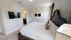 Ein Schlafzimmer mit Bett, einem an der Wand montierten Fernseher, einem Nachttisch mit Lampe und einer Tür zu einem Badezimmer.