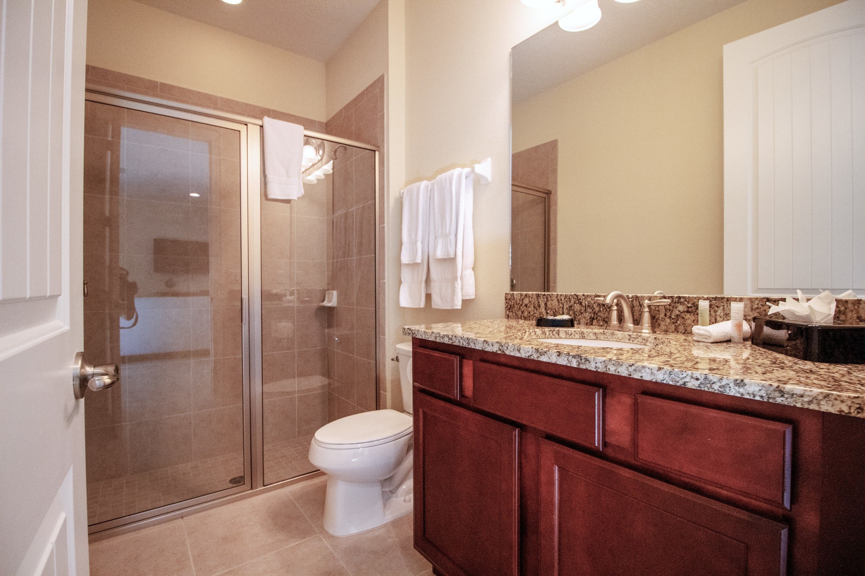 A modern bathroom with a glass shower enclosure, a white toilet, and a vanity with a granite countertop.
