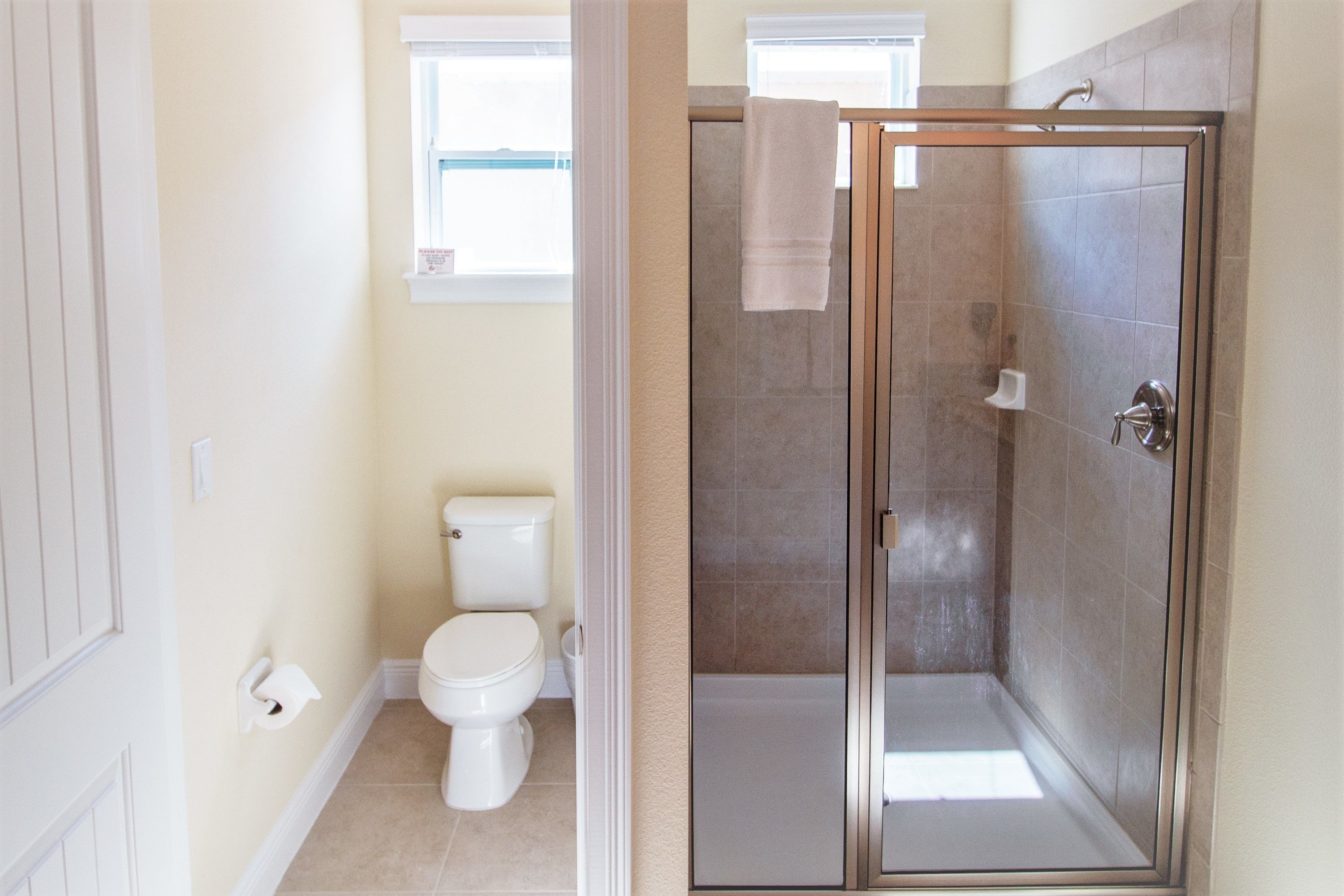 A bathroom with a toilet, a shower with a glass door, and a window above the toilet.