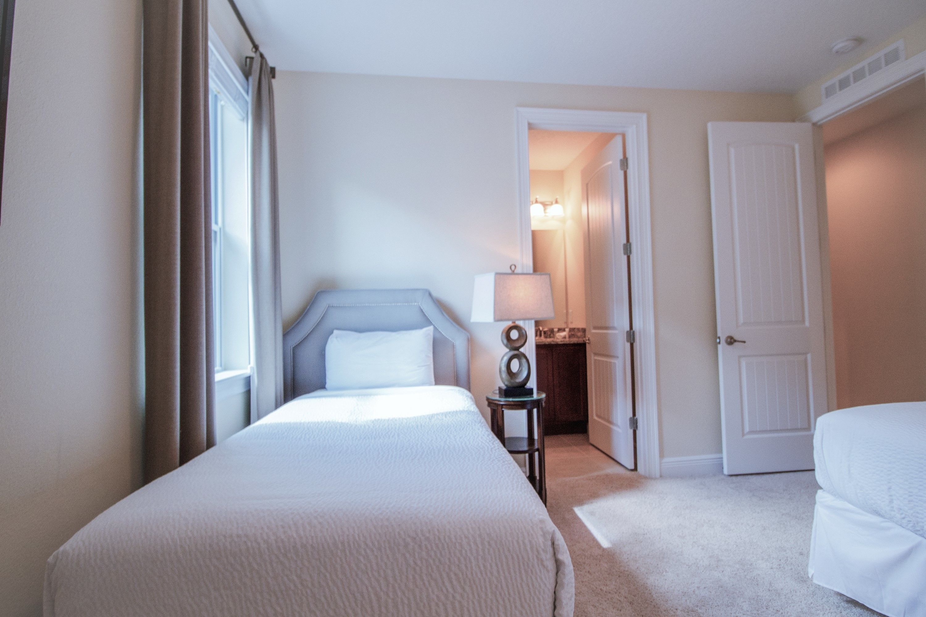 A hotel room with a large bed, a bedside table, a lamp, and a door leading to a bathroom.