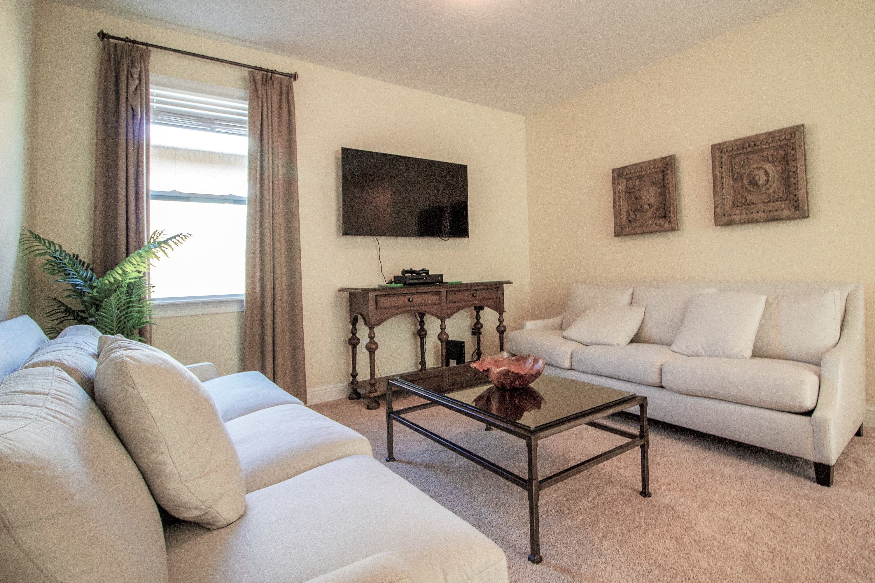 A living room with a beige sofa, a coffee table, a flat-screen TV, and two decorative wall pieces.