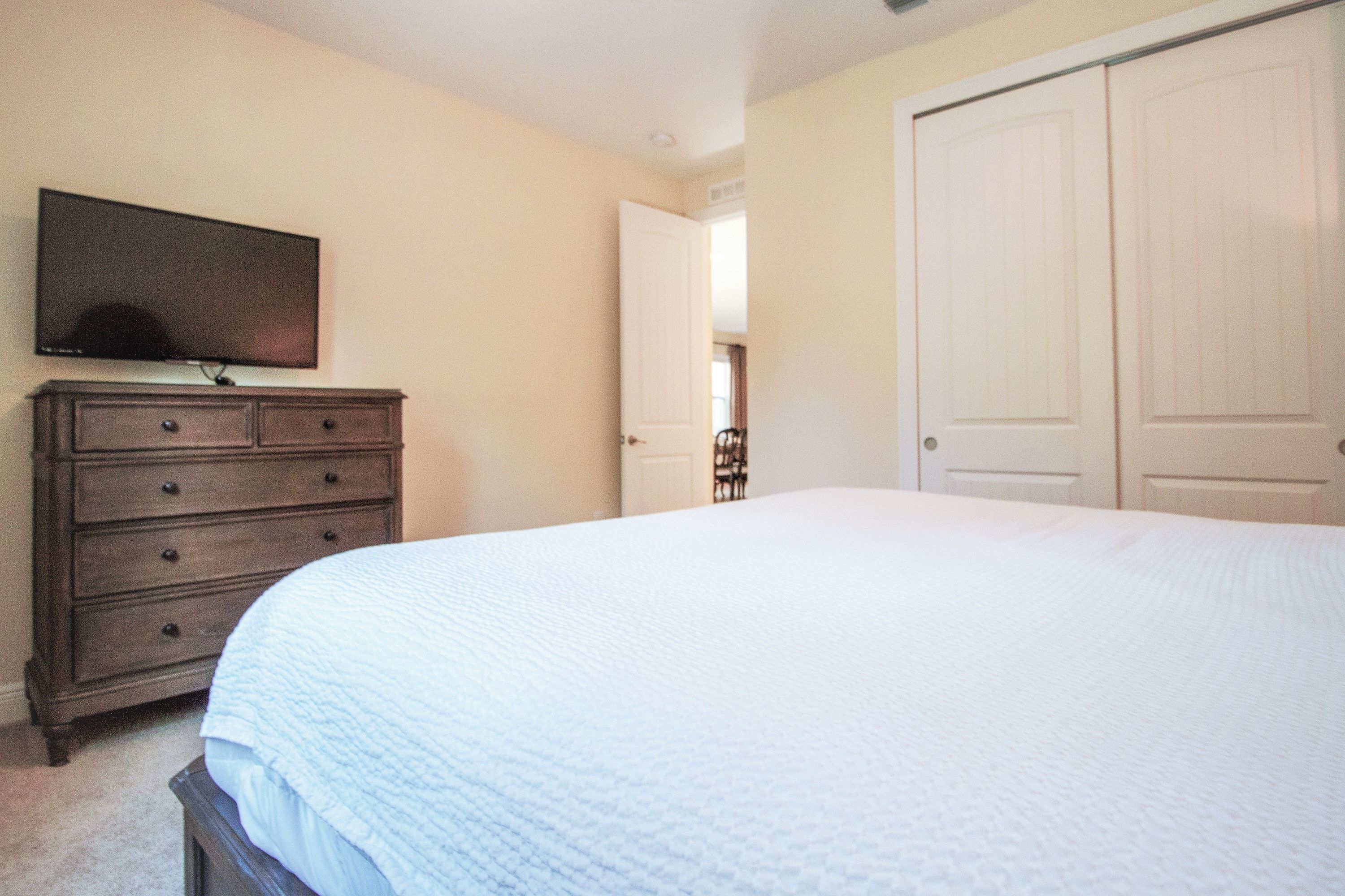 A bedroom with a bed, a dresser, a television, and a closet.