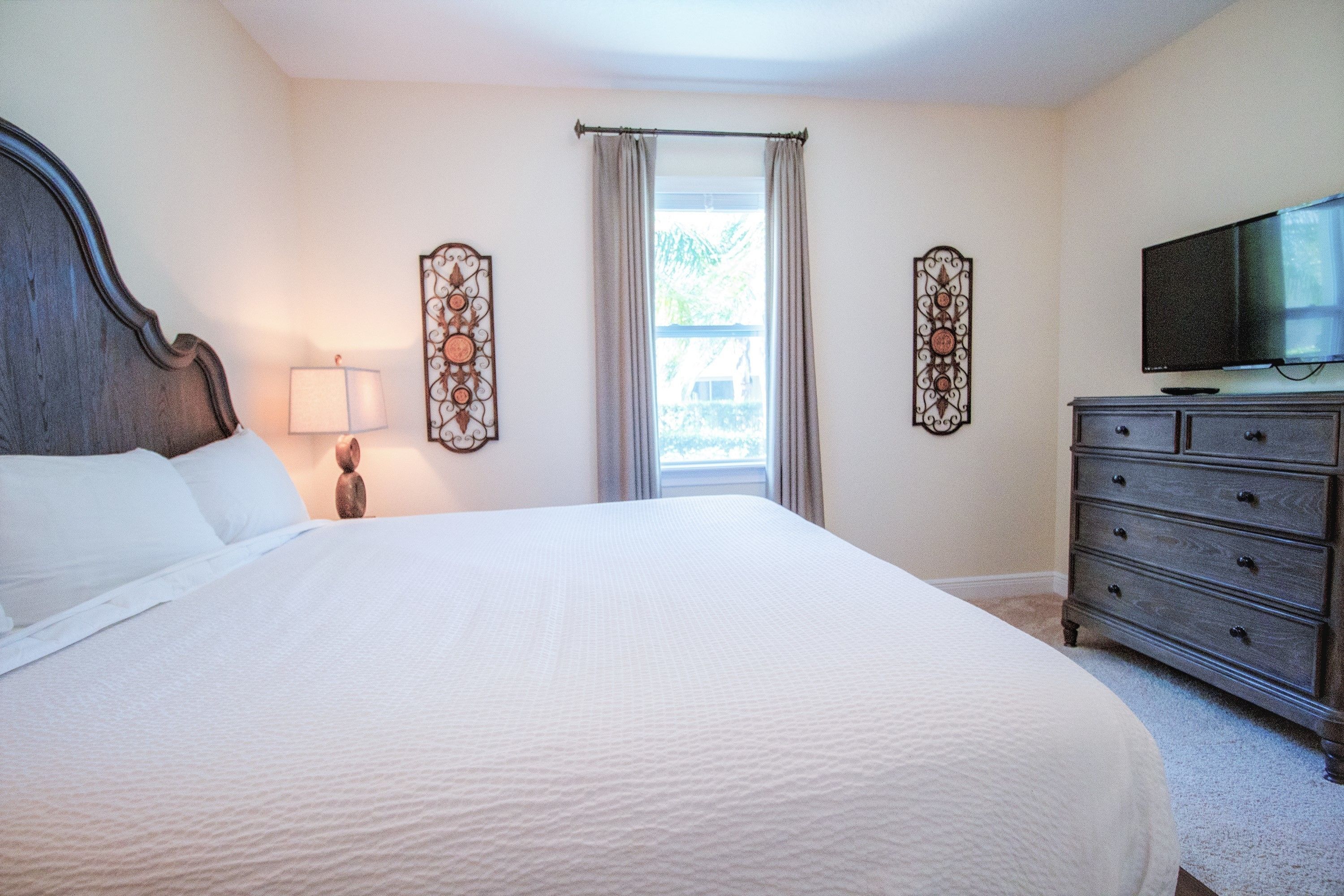 A bedroom with a large bed, a dresser, a television, and decorative wall art.