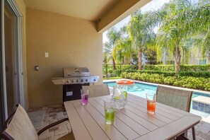 Eine Terrasse im Freien mit Tisch, Stühlen, Grill und Blick auf einen Pool.