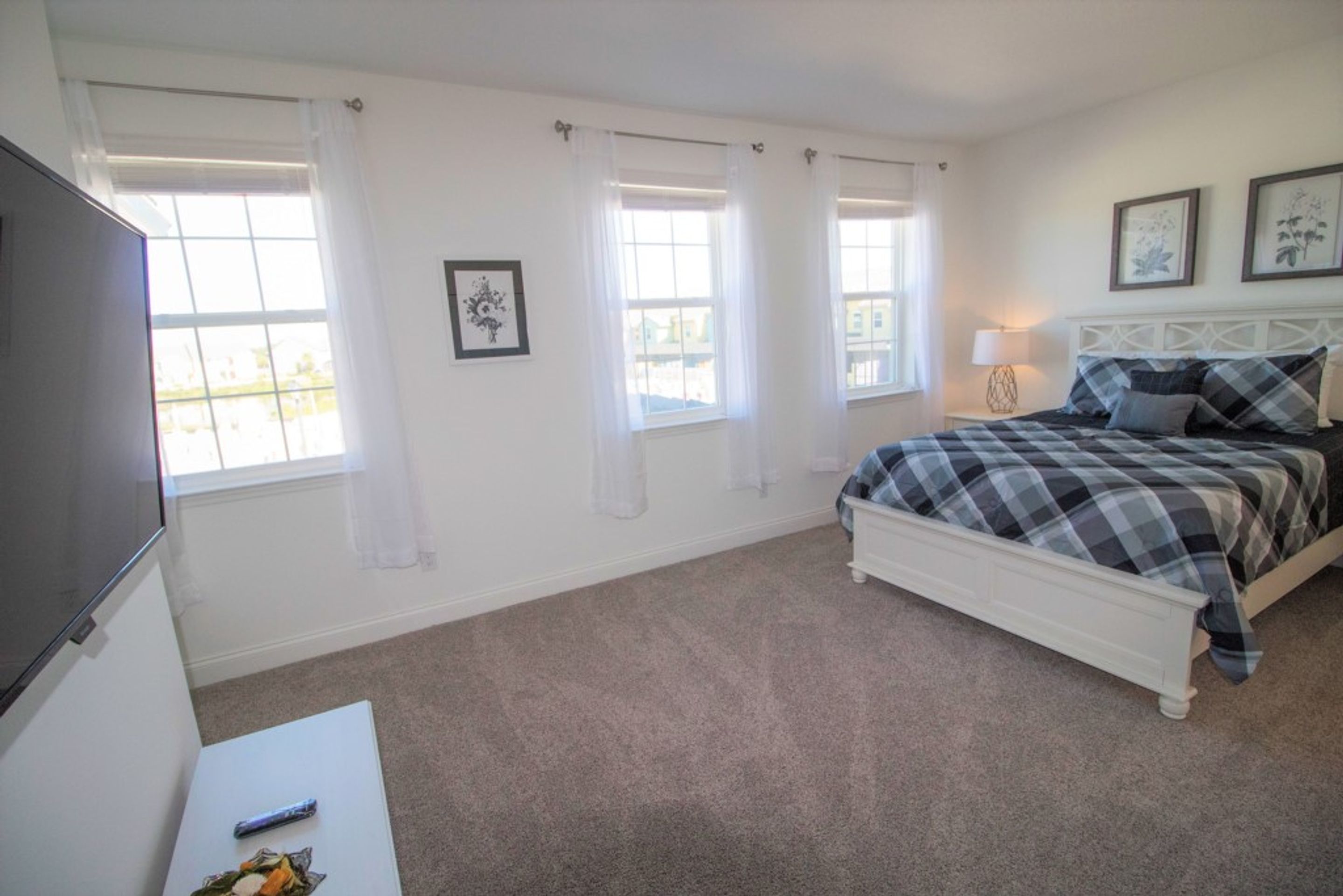 A bedroom with a bed, a TV, and two windows with curtains.
