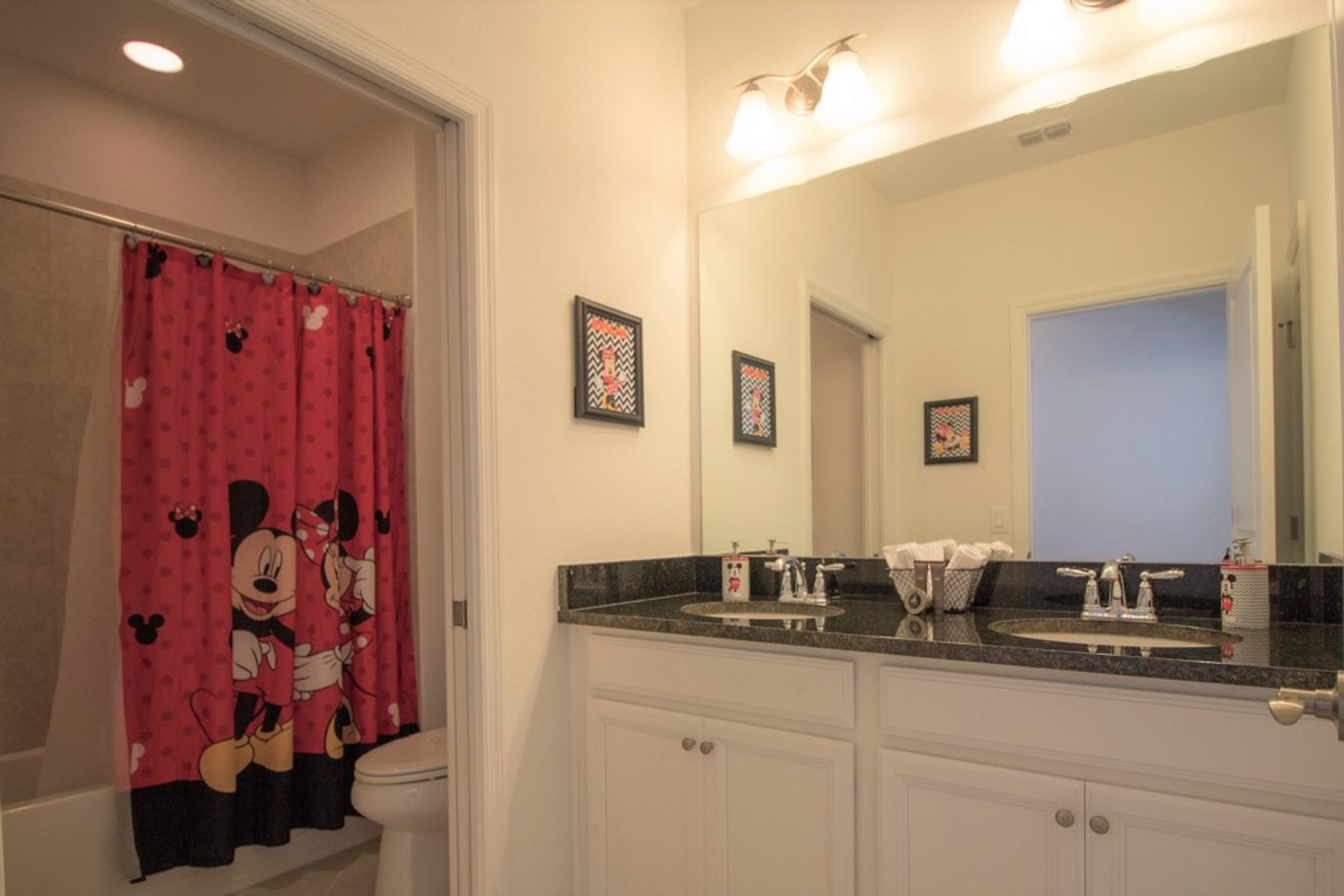 Een badkamer met een Mickey Mouse douchegordijn, een dubbele wastafel en een grote spiegel.