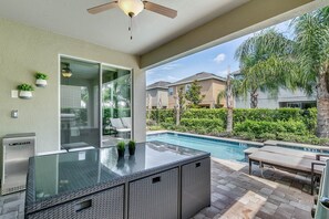 An outdoor patio with a glass-top table, wicker furniture, and a pool. - Encore Resort at Reunion 7605 (Kissimmee)
