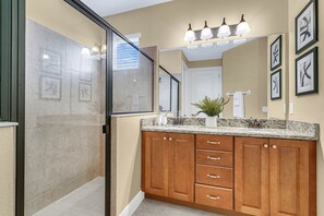 A modern bathroom with a glass shower enclosure, wooden cabinets, and a granite countertop. - Encore Resort at Reunion 7605 (Kissimmee)