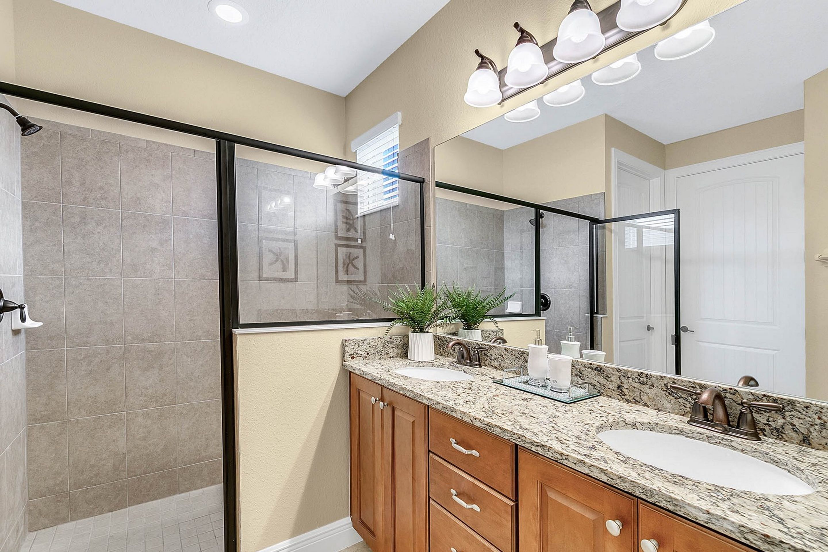 A modern bathroom with a walk-in shower, a large mirror, and a granite countertop.