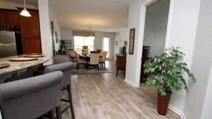 A modern kitchen with a central island, bar stools, and a dining area with chairs and a table. - Vista Cay 4840 - 108 (Orlando)