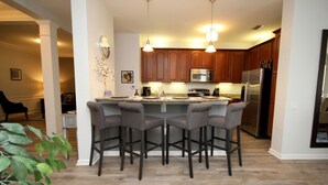 A modern kitchen with wooden cabinets, stainless steel appliances, and a central island with bar stools. - Vista Cay 4840 - 108 (Orlando)