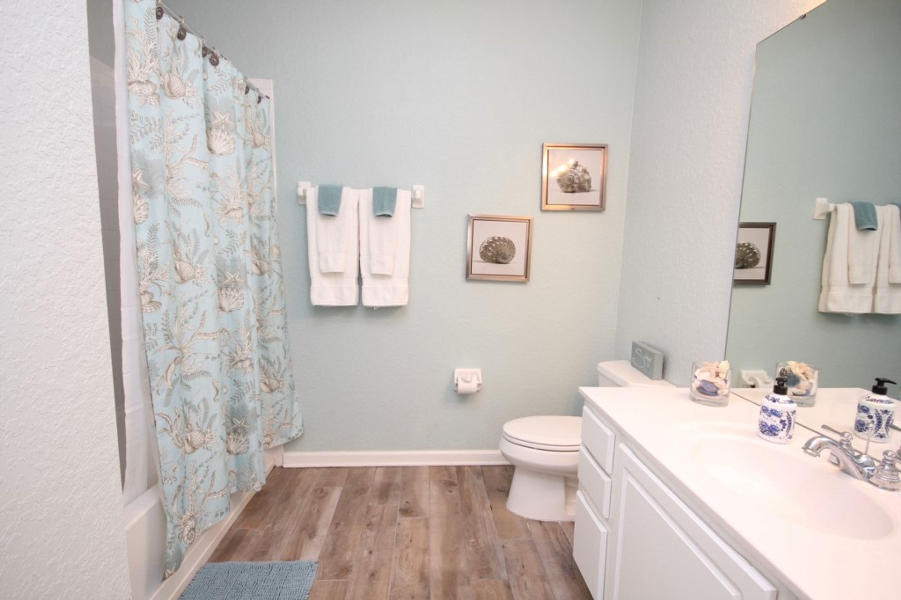 A bathroom with a shower curtain, toilet, sink, and two framed pictures on the wall.