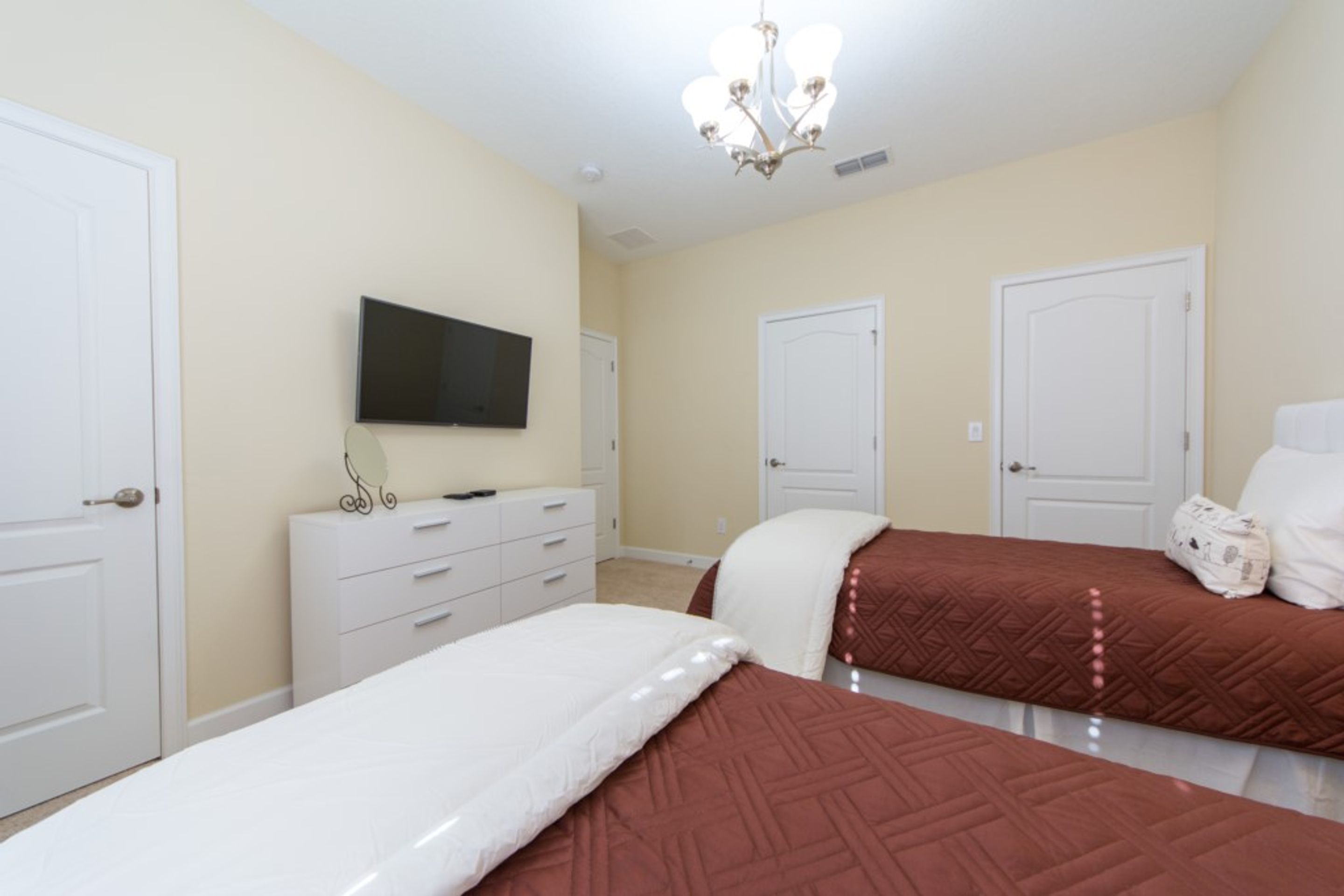 Une chambre avec deux lits, une télévision, une commode et un lustre.