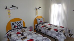 Ein Schlafzimmer mit zwei Betten, jeweils mit Bettbezügen im Minnie Mouse Design. An den Wänden befinden sich Delfin-Dekorationen und ein Fenster mit Vorhängen.