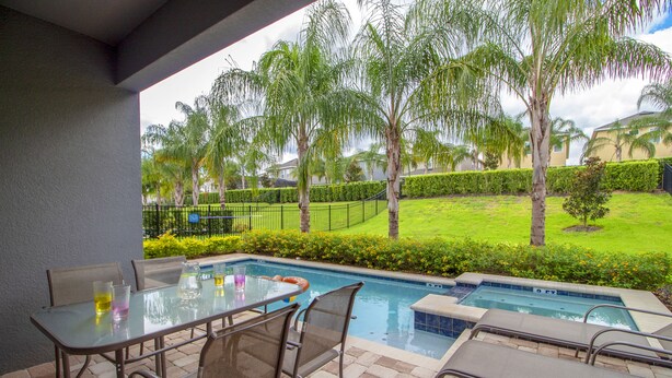 An outdoor pool area with a glass table and chairs, surrounded by palm trees and a well-maintained lawn. - Encore Resort at Reunion 7500 (Kissimmee)