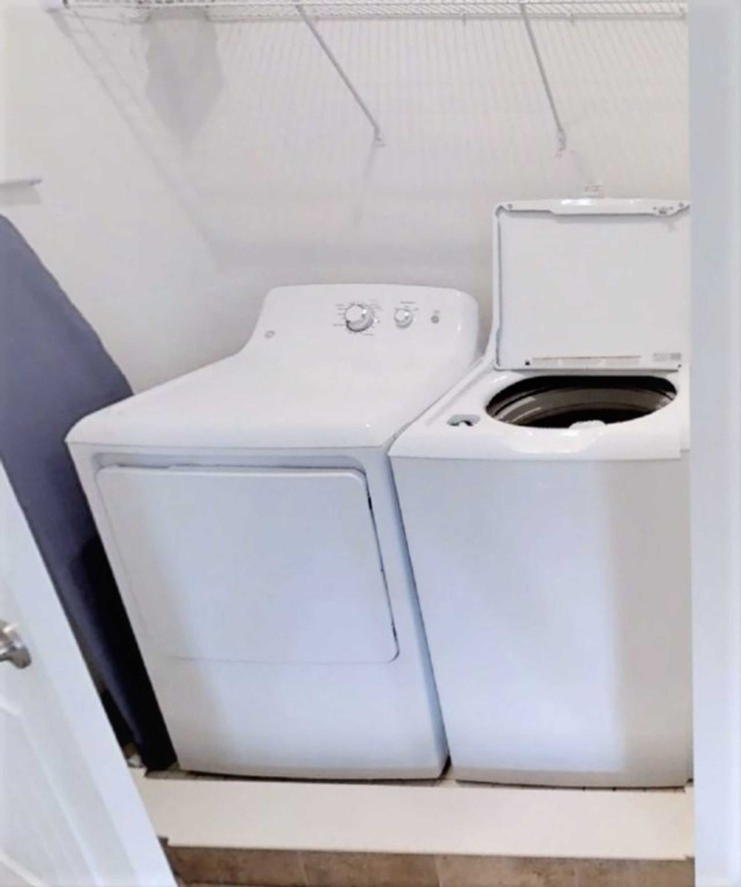 A compact, white laundry room with a front-loading washer and dryer, a tiled floor, and a metal rack above the dryer.