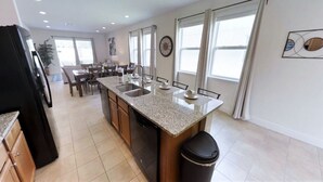 A modern kitchen with granite countertops, a dishwasher, and a dining area with a table and chairs. - Encore Resort at Reunion 7500 (Kissimmee)