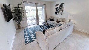 A modern living room with a white sofa, a coffee table, and a large potted plant. - Encore Resort at Reunion 7500 (Kissimmee)