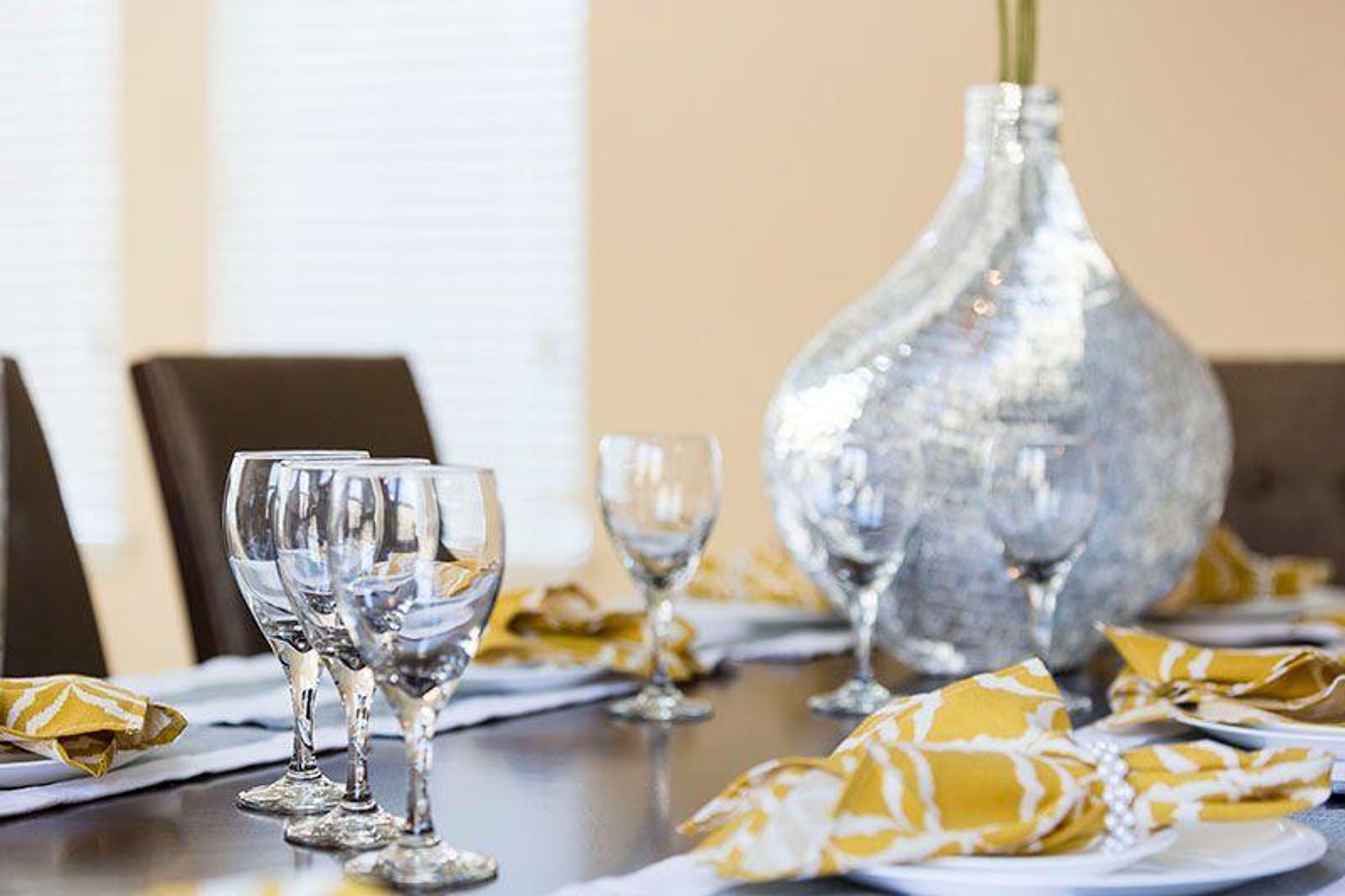 A dining table set with multiple wine glasses, a silver vase, and yellow napkins.