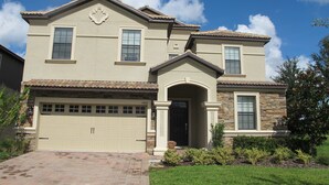 A two-story house with a beige facade, a stone accent wall, and a garage. - Champions Gate 1400 (Davenport)
