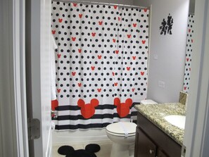 Ein Badezimmer mit einer Mickey Mouse Duschvorhangs, einer gestreiften Dekoration mit Mickey Mouse Kopf und einem Waschbecken mit einer Granit-Arbeitsplatte.