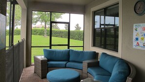 A covered patio area with a blue sectional sofa and a round ottoman. - Champions Gate 1400 (Davenport)