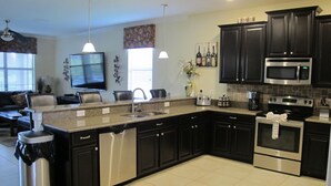 A modern kitchen with dark cabinetry, stainless steel appliances, and a central island. - Champions Gate 1400 (Davenport)