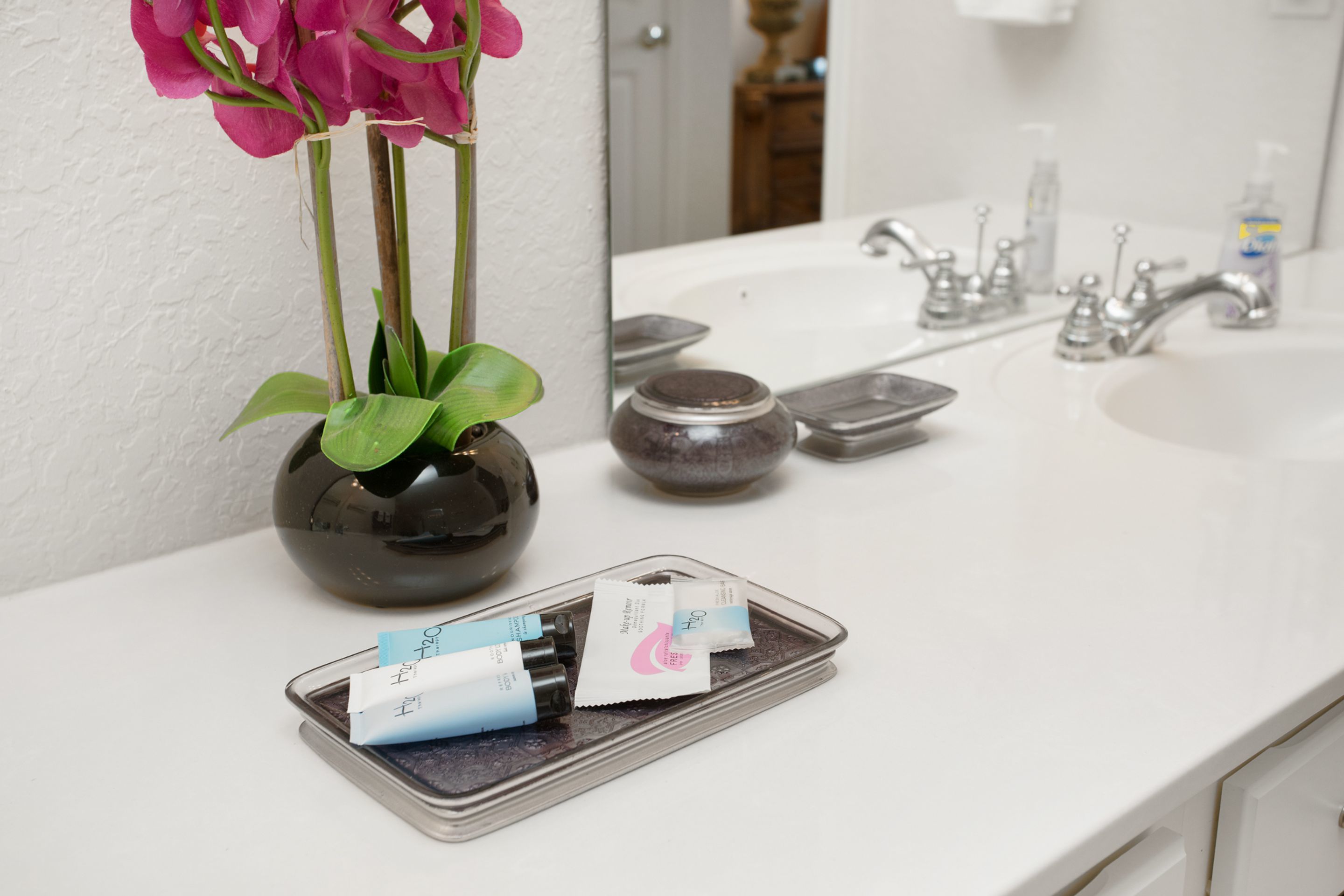 Un baño con un lavamanos blanco, un espejo y un florero con flores rosas.