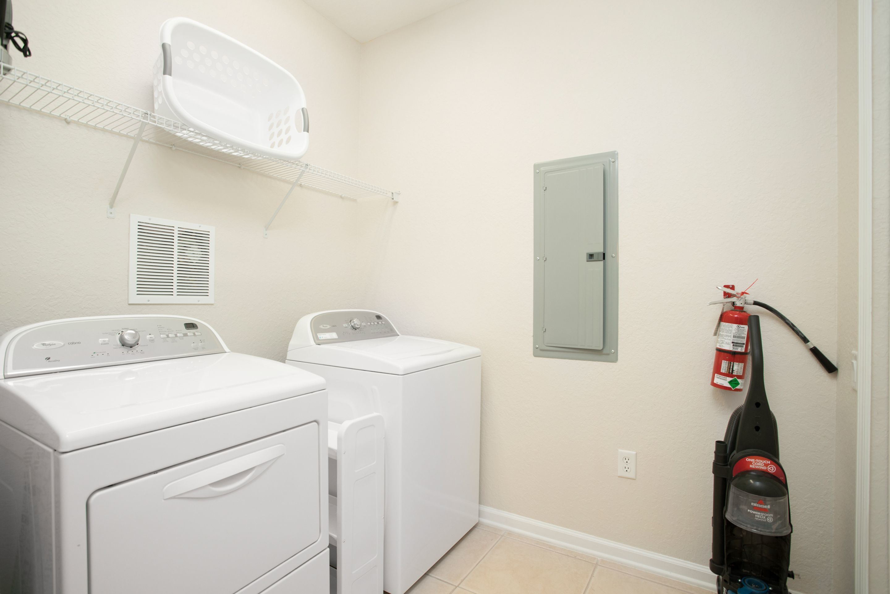 A laundry room with two white front-loading washers and dryers, a white drying rack, a fire extinguisher, and a vented cabinet.
